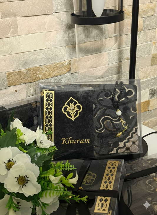 Personalized Islamic gift set in black and gold featuring a custom-embroidered velvet Surah book with custom name of your choice, an adult-size travel prayer mat with damask pattern, and a black tasbih in a clear PVC gift box.